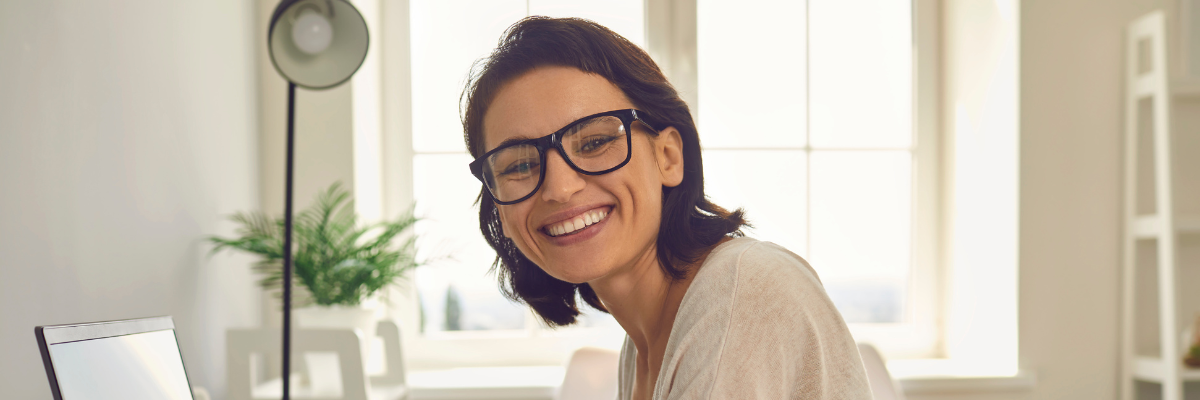 uśmiechnięta kobieta w okularach przed laptopem